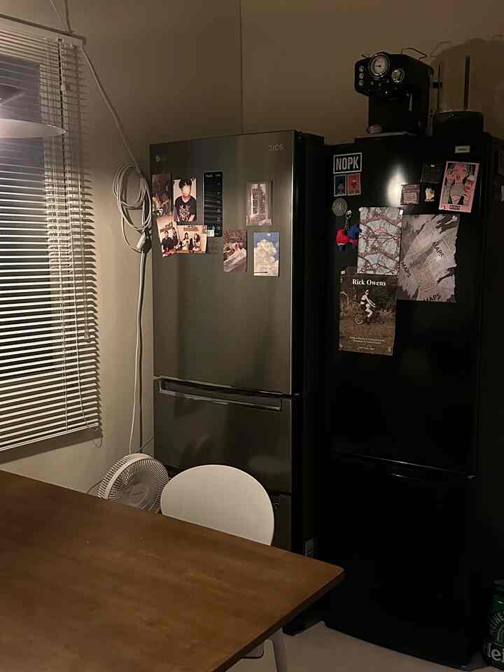 温かみのあるブラウンのダイニングテーブル、白い椅子、写真が貼られた2台の冷蔵庫が配置された落ち着いたキッチンスペース