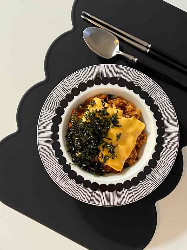 黒のランチョンマットに柄入りの白いボウルとカトラリーが置かれた清潔な食事空間