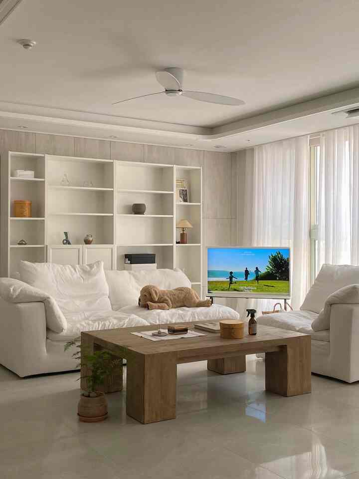 ホワイトと木目調が調和するリビング、広いホワイトソファと木製コーヒーテーブルが配置された落ち着いた温かみのあるインテリア