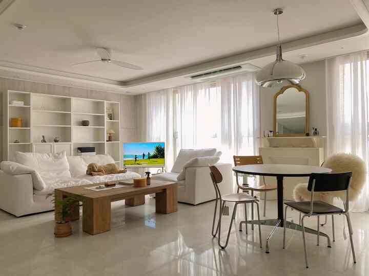 明るく広々とした白とナチュラルカラーのリビングとダイニング、ソファと丸いダイニングテーブルが配置された落ち着いた空間