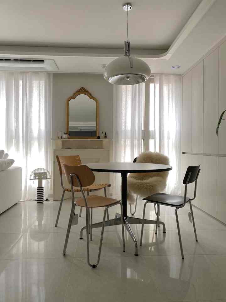 白と木目調が調和したダイニング、円形テーブルとヴィンテージの金色の鏡が配置された洗練された空間