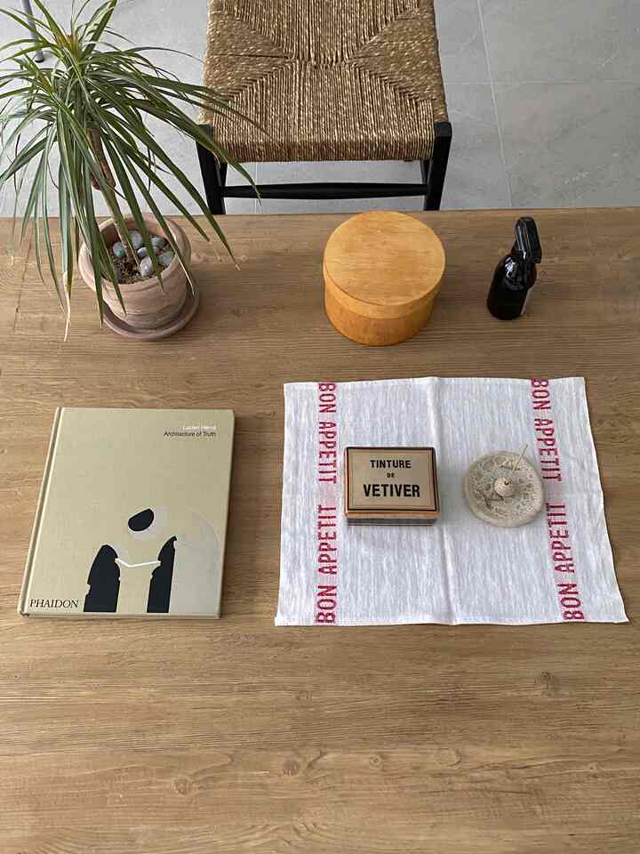 ナチュラルで木目調のテーブルの上に植物、木製の容器、ランチョンマット、本が配置された雰囲気のあるインテリア