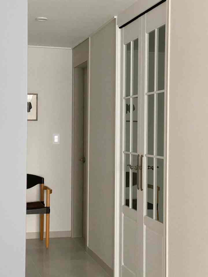 ベージュ色調の縦長の廊下にフレンチスタイルの中間ドアと木製の椅子が配置された、自然でモダンな玄関のインテリア