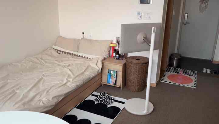 ベージュトーンの寝室、中央に収納ベッドとナイトテーブル、横にラタンハンパーが置かれた雰囲気ある空間