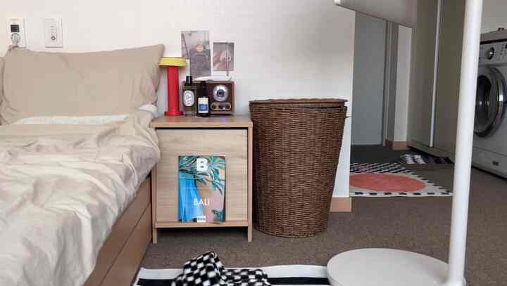 ナチュラルなベージュ色の寝室、木製ナイトテーブルとラタンのハンパーが調和する温かみのあるインテリア