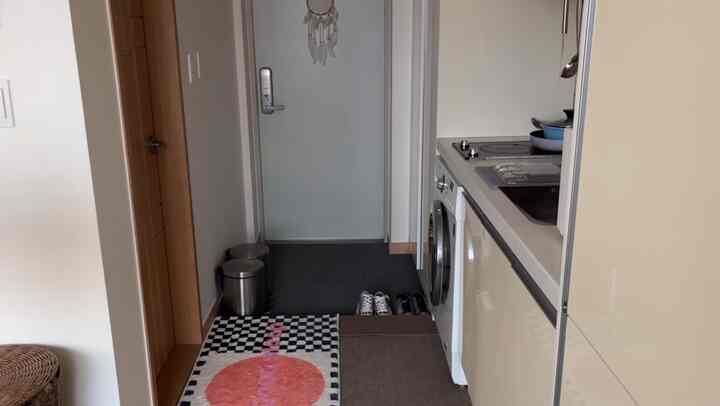 ダークグレーとブラウンの色調の玄関スペース、シューズラックとタイルカーペットが配置された実用的で居心地の良い入口