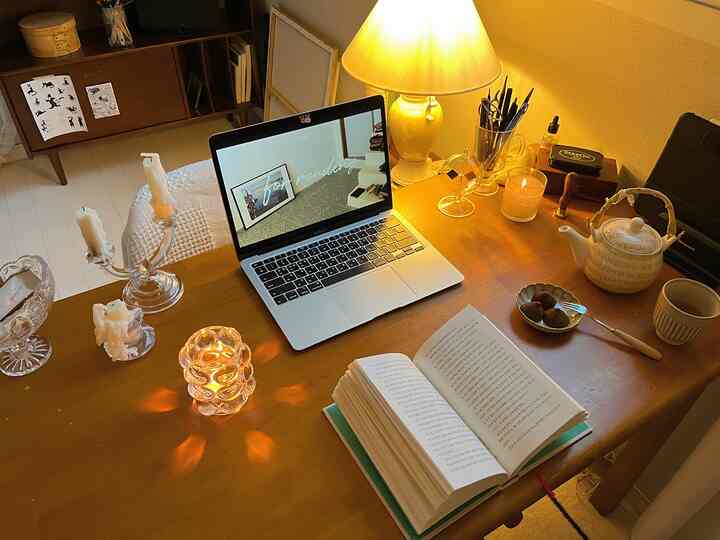 暖かなゴールドとナチュラルカラーのデスクにノートパソコン、キャンドル、ティーポット、本が配置された雰囲気のあるホームカフェ兼在宅勤務空間
