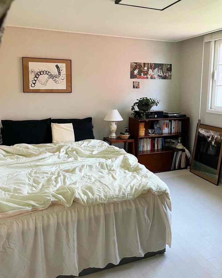 白とナチュラルトーンの寝室、中央にベッドがあり、横に本棚とスタンドランプが配置された落ち着いた空間