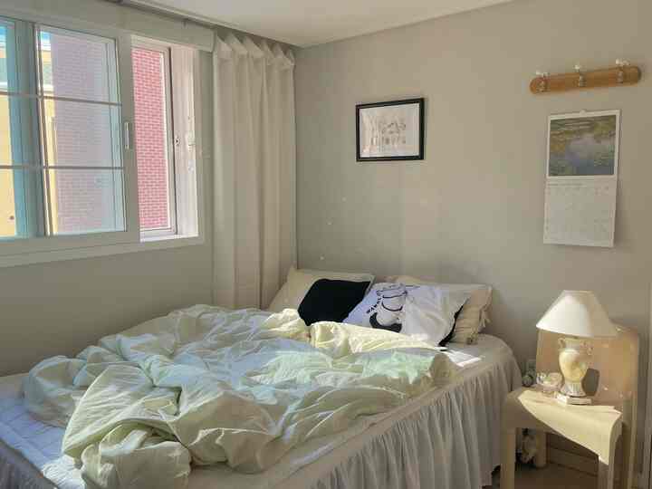 明るく柔らかなアイボリーとホワイト調の寝室、窓際のベッドとナイトテーブル、カーテンが調和する落ち着いた空間