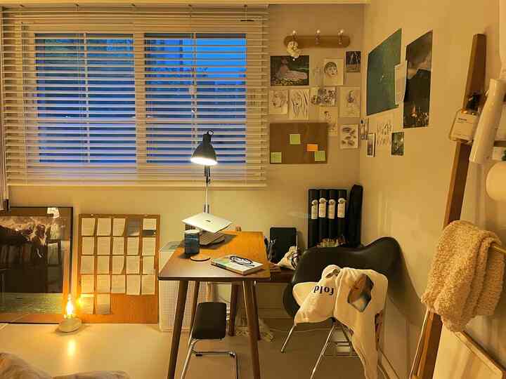 温かみのあるウッドトーンとベージュ色の照明が調和したホームオフィス、壁面には様々なポスターとアートワークが飾られている