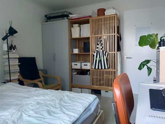 白い壁とナチュラルな木製家具が配置された一人暮らしの寝室、ホームオフィスがある清潔で居心地の良い空間