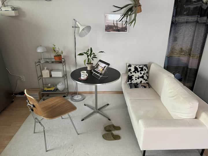 ホワイトとブラックのトーンでまとめられたモダンな一人暮らしのリビング、ソファと丸テーブル、木製チェアが配置された清潔感のある空間