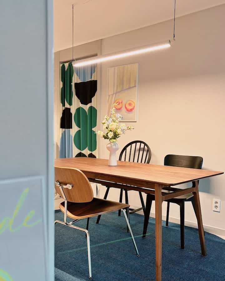 ブラウンの木製ダイニングテーブルとブルーカーペット、柄のカーテンが配置されたナチュラルモダンなダイニングルーム