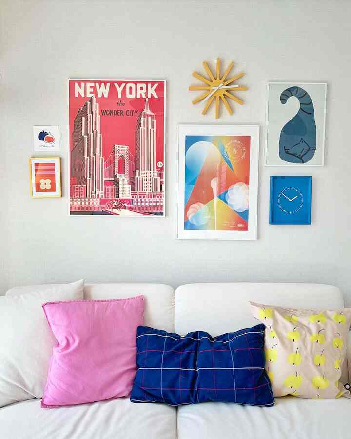 白を基調としたリビング、白いソファにピンク、ブルー、黄色のクッションが配置され、ホームギャラリー風の壁面インテリア