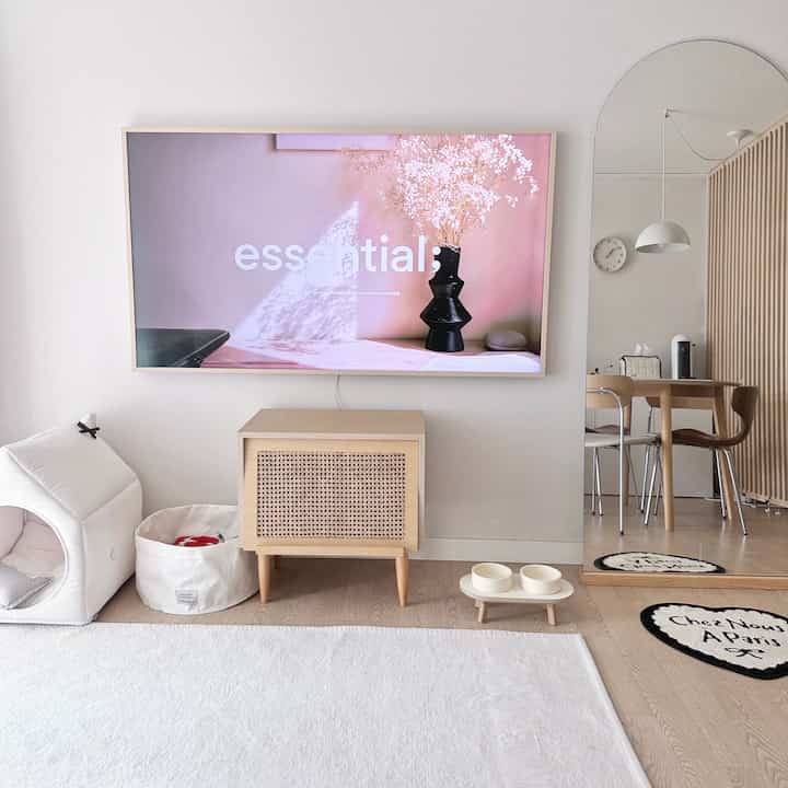 白と木目調が調和したリビングルーム、テレビと木製キャビネット、ペットハウスと食器セットが配置された清潔感のある空間