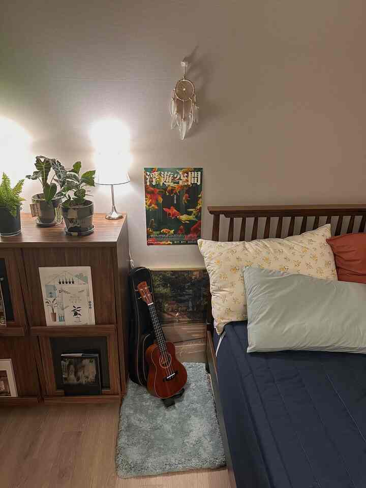 ネイビーのベッドカバーと木製フレームが調和するアットホームな寝室、植物とナイトスタンドランプが配された落ち着いた空間