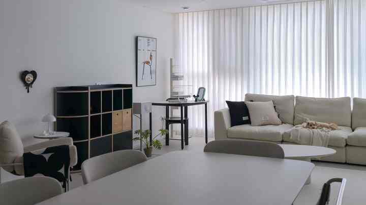 白とベージュ、黒のトーンのリビング、広いコーナーソファとダイニングテーブルが配置された落ち着いたモダンなインテリア