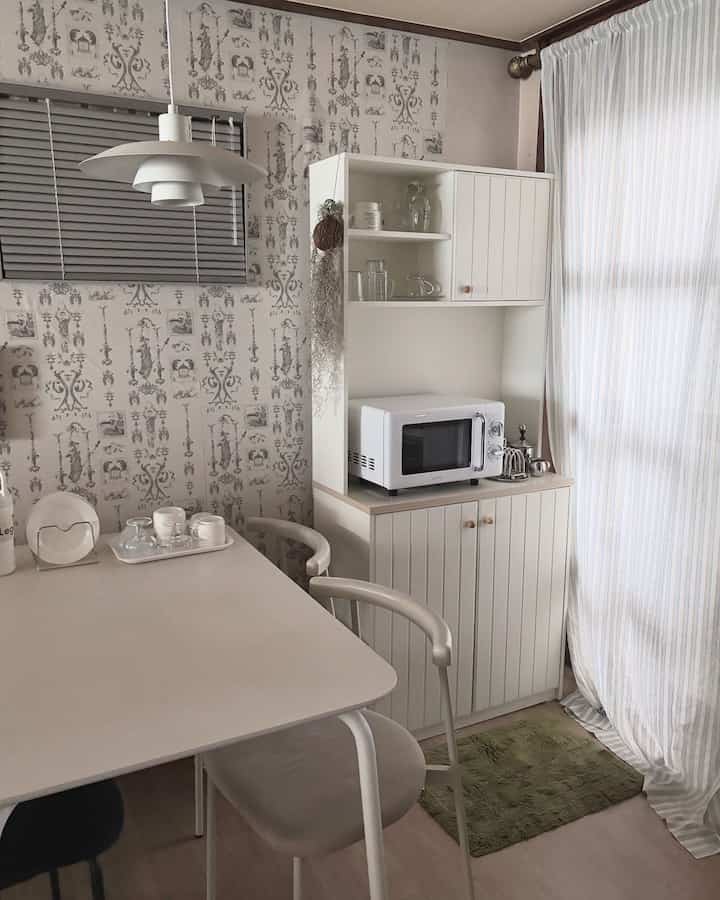 ホワイトとアイボリーのトーンでまとめられた、ダイニングテーブルとカーテン、キャビネットが配置された明るくモダンなキッチンスペース