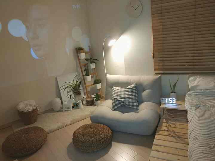 White and wood tone studio apartment bedroom-living space featuring sofa, rug, and a projector creating a cozy atmosphere
