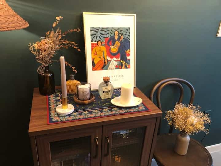 Brown cabinet and chair against a dark gray wall, decorated with a framed picture, candles, and vases creating a cozy interior