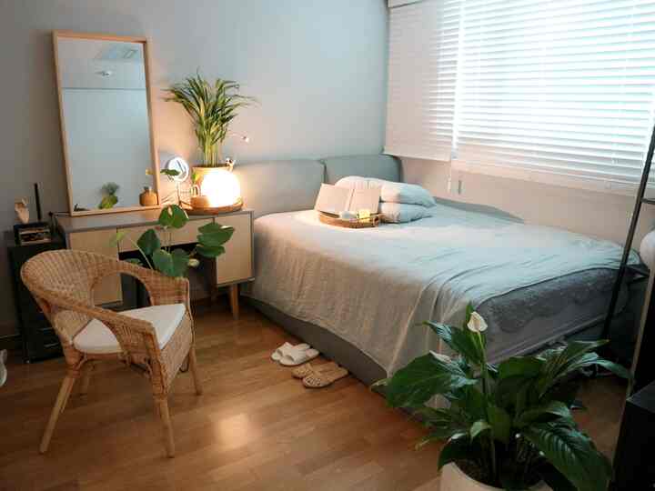 ナチュラルカラーと木目調の寝室、ラタンチェアとベッド、植物が配置された落ち着いた印象の空間