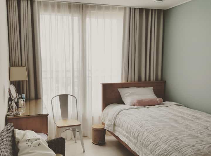 Beige and white toned bedroom featuring wooden bed and linen curtains with a calm ambiance