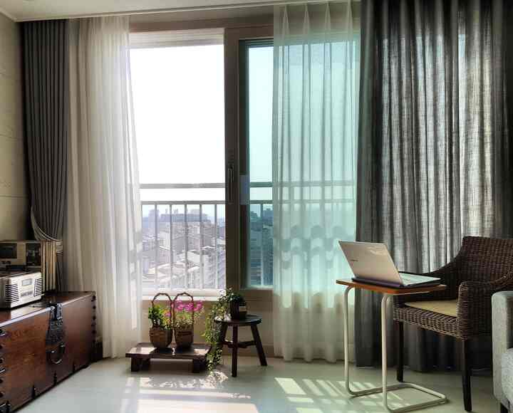 ホワイトの床とブラウンの家具があるナチュラルスタイルのリビング、窓辺に植物とアームチェアが配置された落ち着いた空間