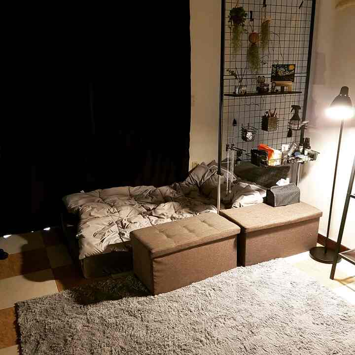 暗い黒いカーテンとブラウンのスツール、グレーの寝具が配置された小さなワンルームの寝室