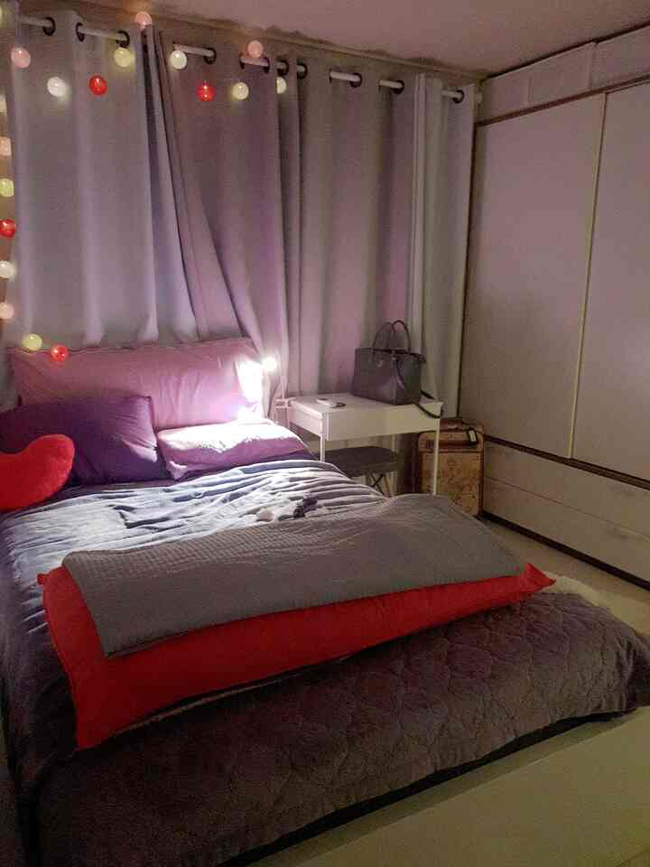 グレーとパープル、ホットピンクの色調の寝室、ベッドと遮光カーテン、コットンボールライトが配置された居心地の良いインテリア