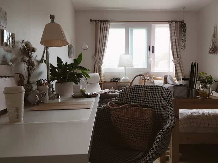 A cozy bedroom with natural tones and wood furniture, featuring a desk and an armchair arranged for comfort