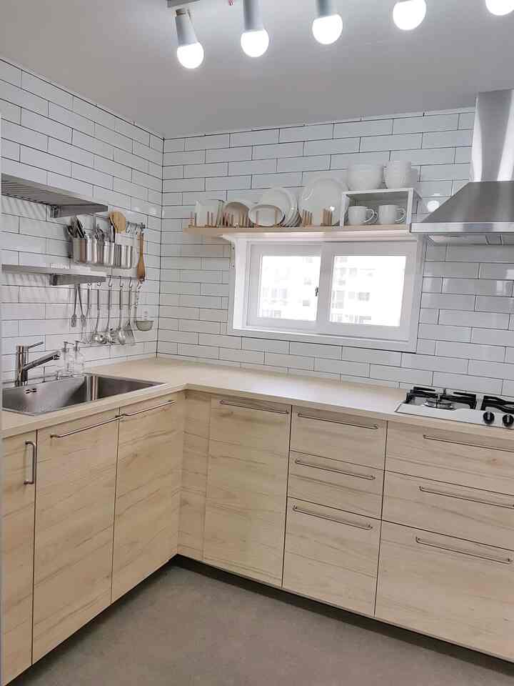 Light wood-tone lower cabinets and shelves with white tile backsplash create a natural, airy and compact kitchen space