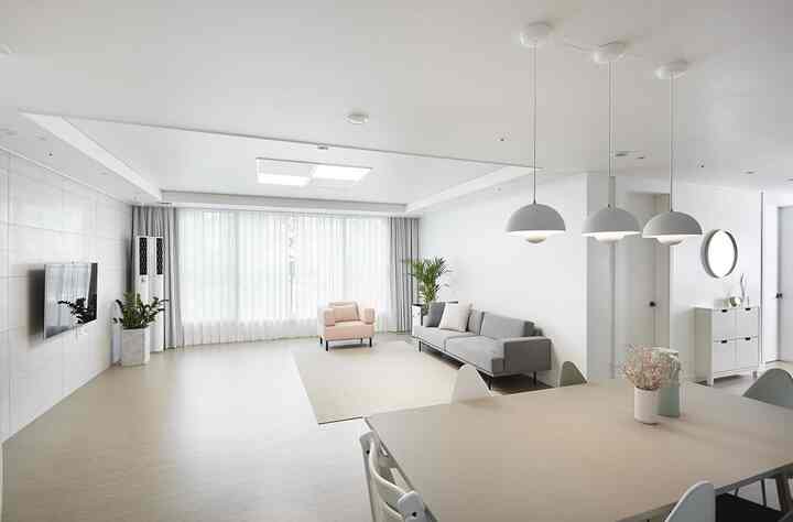 ホワイトとグレーのトーンのミニマルなリビング、グレーのソファとライトピンクのアームチェア、ラグとペンダントライトが調和した空間