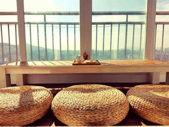 Natural-toned veranda featuring round woven stools and wooden bench with coffee tray, creating a cozy morning vibe
