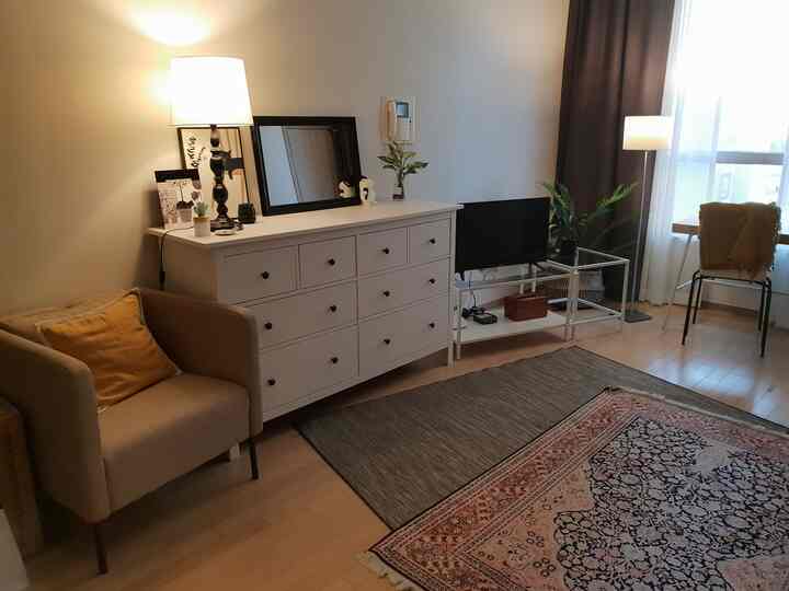 White and wood tone living room featuring a large dresser, armchair, and a desk with lighting near the window creating a cozy atmosphere
