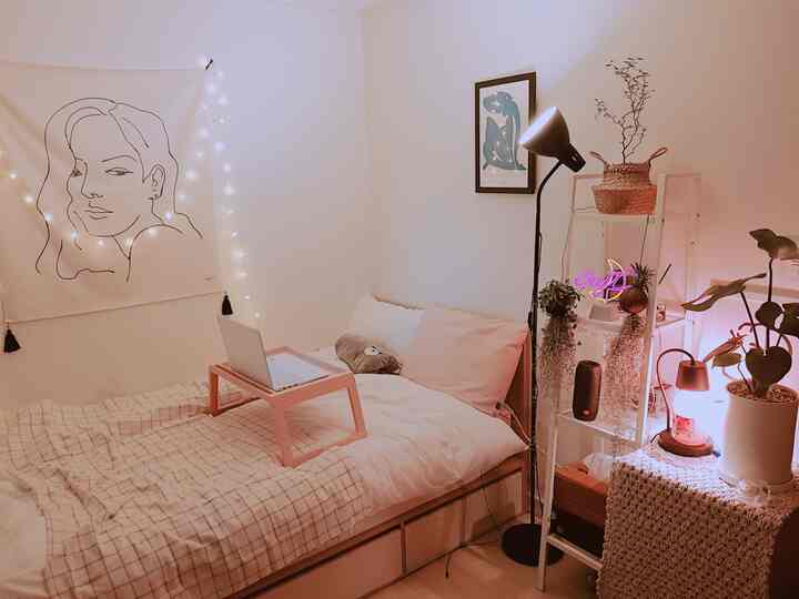 白とベージュのトーンの寝室、中央にベッドが配置され、ノートパソコン用のテーブルと多様な照明がある雰囲気の良いインテリア