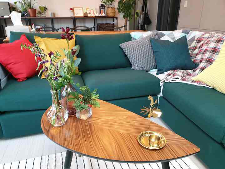 Wood tone living room featuring green sofa with colorful cushions, dried flowers, and gold decorative piece creating a cozy atmosphere