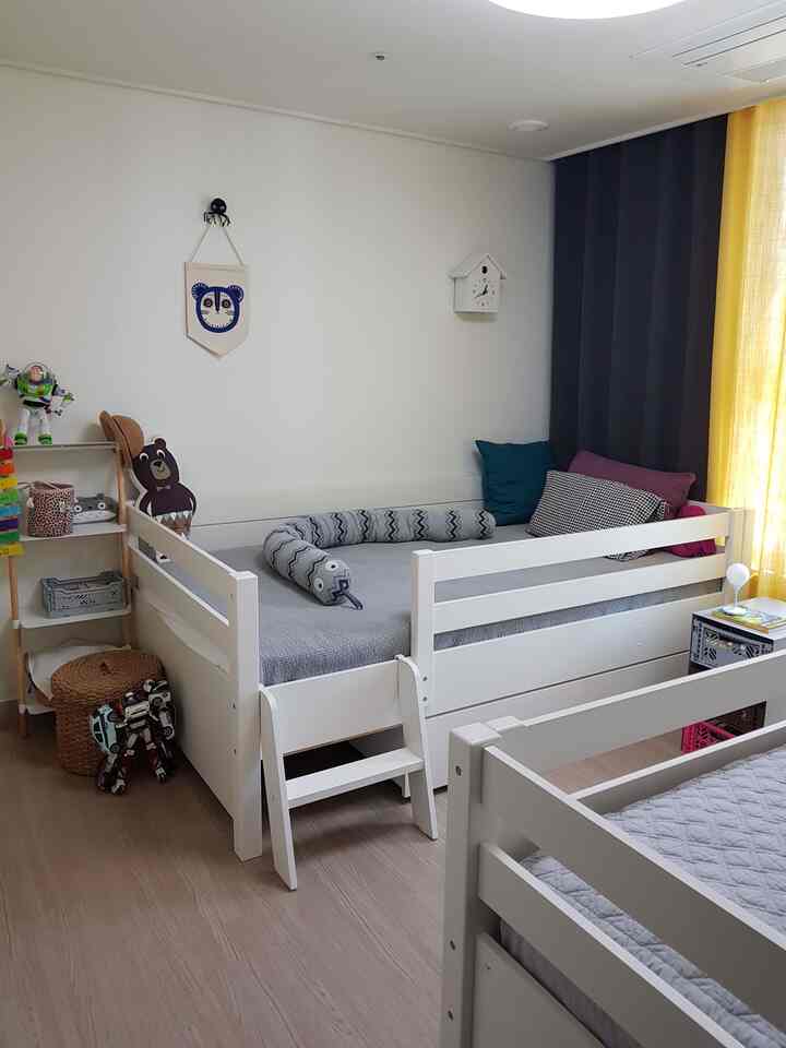 White and gray toned kids' bedroom featuring two white beds, toys, cushions, and a clock in a neat setting