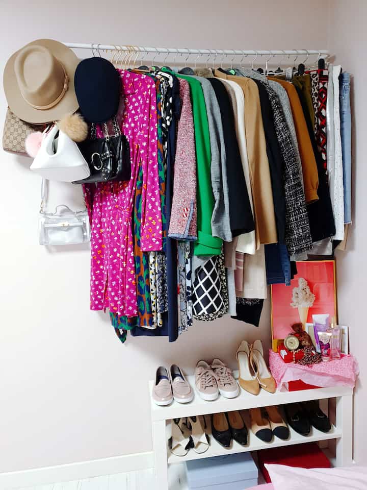 白い壁と床が調和する小さなクローゼット空間、ハンガーラックに多彩な冬服と帽子が掛けられ、下部に整頓されたシューズラックがある雰囲気のあるインテリア