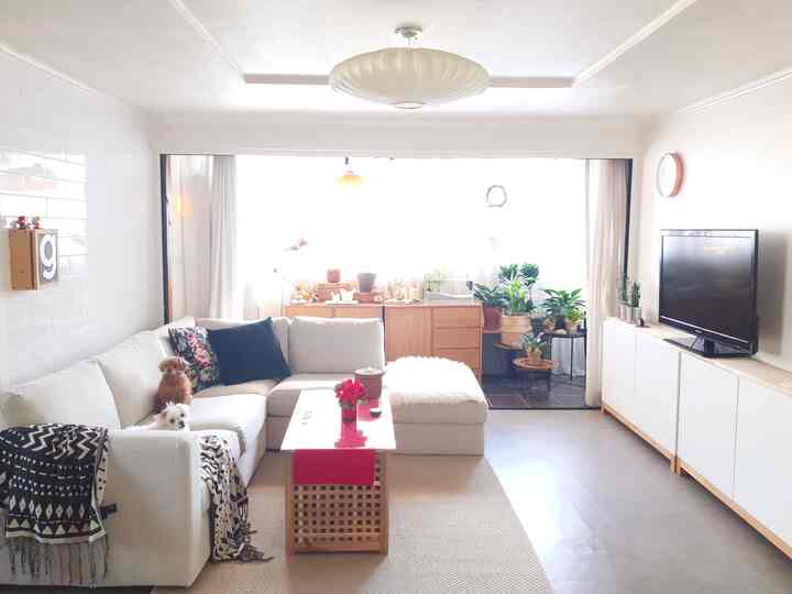 Bright white and beige wood-toned living room featuring sectional sofa, veranda with plants and white curtains creating cozy atmosphere