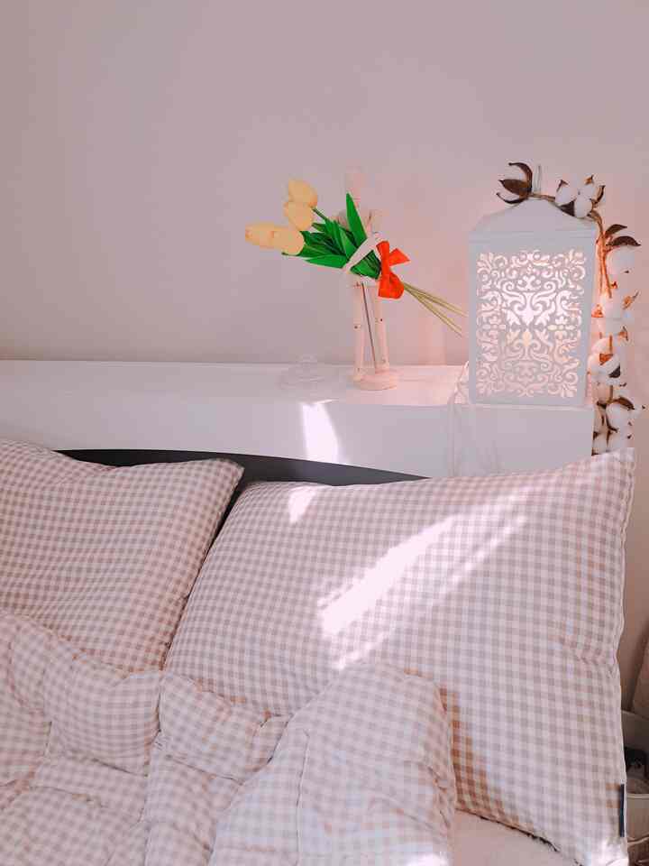 Beige checkered bedding in a cozy bedroom, featuring tulip artificial flowers and a candle warmer on a shelf, creating a natural atmosphere