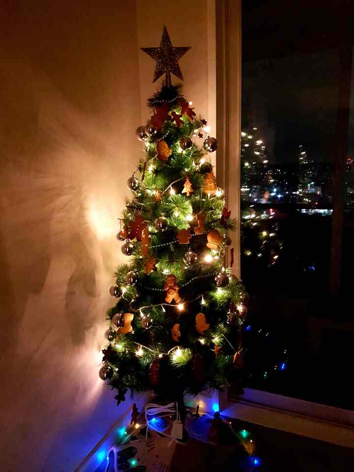 Warm gold and green toned living room featuring a Christmas tree decorated with cookie ornaments and glowing string lights