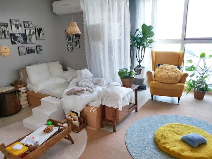 White and yellow-toned studio living room featuring natural wood furniture and plants in a cozy atmosphere