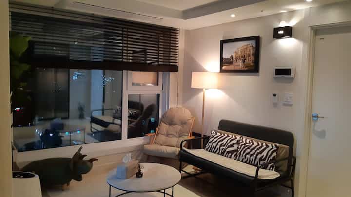 ホワイトの壁とブラウンのブラインドが調和するモダンな狭いリビング、リクライナーとソファベッドが配置された落ち着いた空間