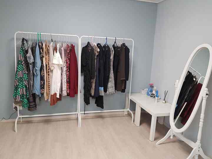 淡いブルーの壁と白い家具が配置されたウォークインクローゼット、洋服ラックに様々な衣類が掛けられた整った空間