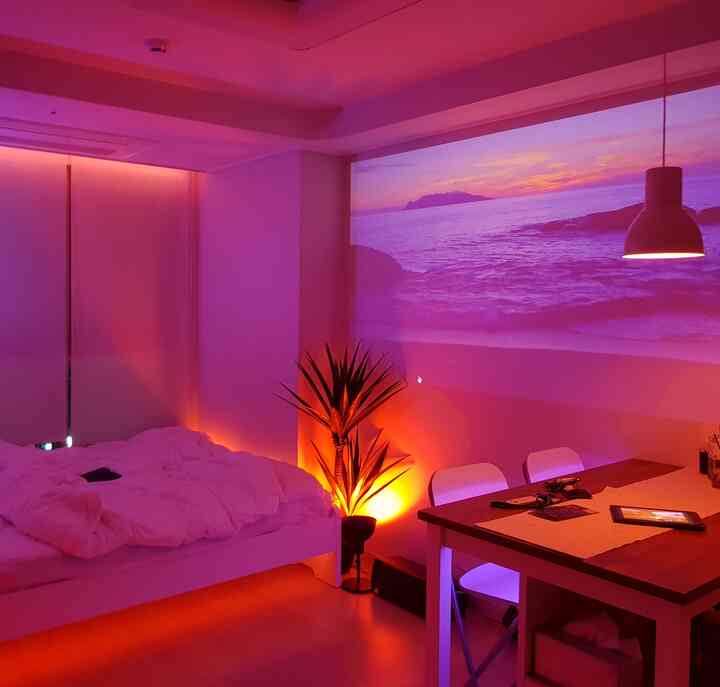 Purple and orange mood-lit studio bedroom featuring white furniture and bedding with a cozy atmosphere