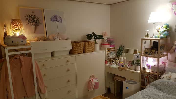 白とピンクのトーンの子供部屋、ドレッサーと収納キャビネットが配置された温かみのある空間