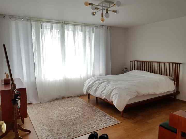 A bedroom featuring white and wood tones, with an elegant bed frame, large window curtains, and a rug creating a cozy atmosphere.