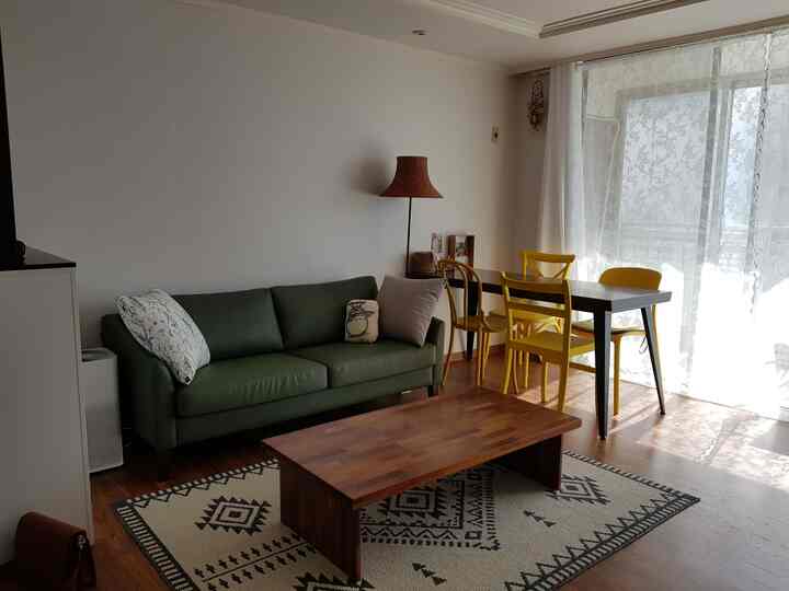 白い壁と木目調の床が調和したリビング、緑のソファと黄色いダイニングチェアが配置された自然光あふれる雰囲気のあるインテリア