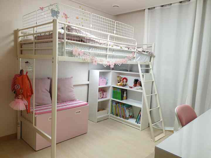 White and pink toned kids' room featuring a bunk bed, bookshelf, and curtains with a cozy atmosphere