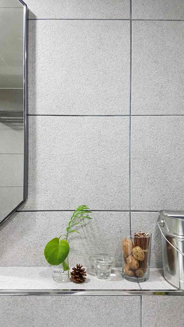 Light gray tiled wall bathroom shelf featuring glass vases with monstera and table palm stems and rustic natural accessories